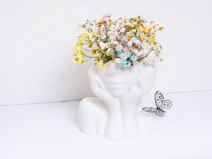 Vase décoratif en forme de visage avec fleurs colorées et papillon pour une ambiance zen et apaisante. Image de l'apaisement mental et physique.